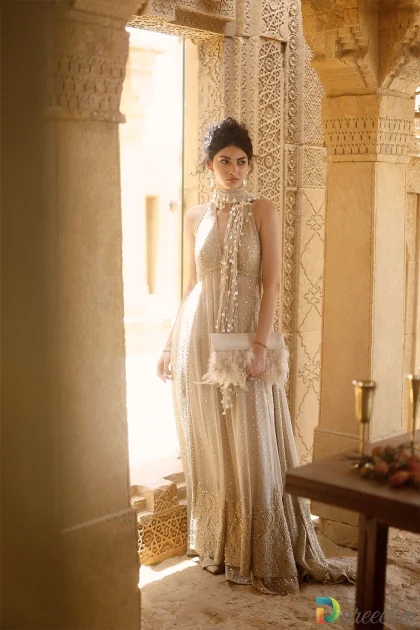 Full length standing portrait of model in beige crinkle chiffon lehenga holding matching feather trim clutch