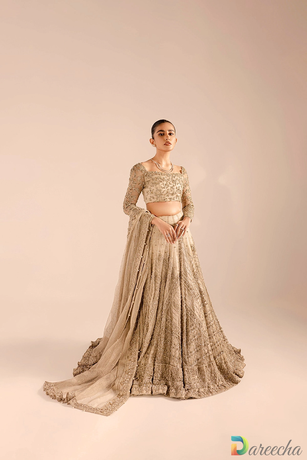 Standing view of model inchampagne kundan bridal lehengaholding draped mukesh work dupatta with pearl edging