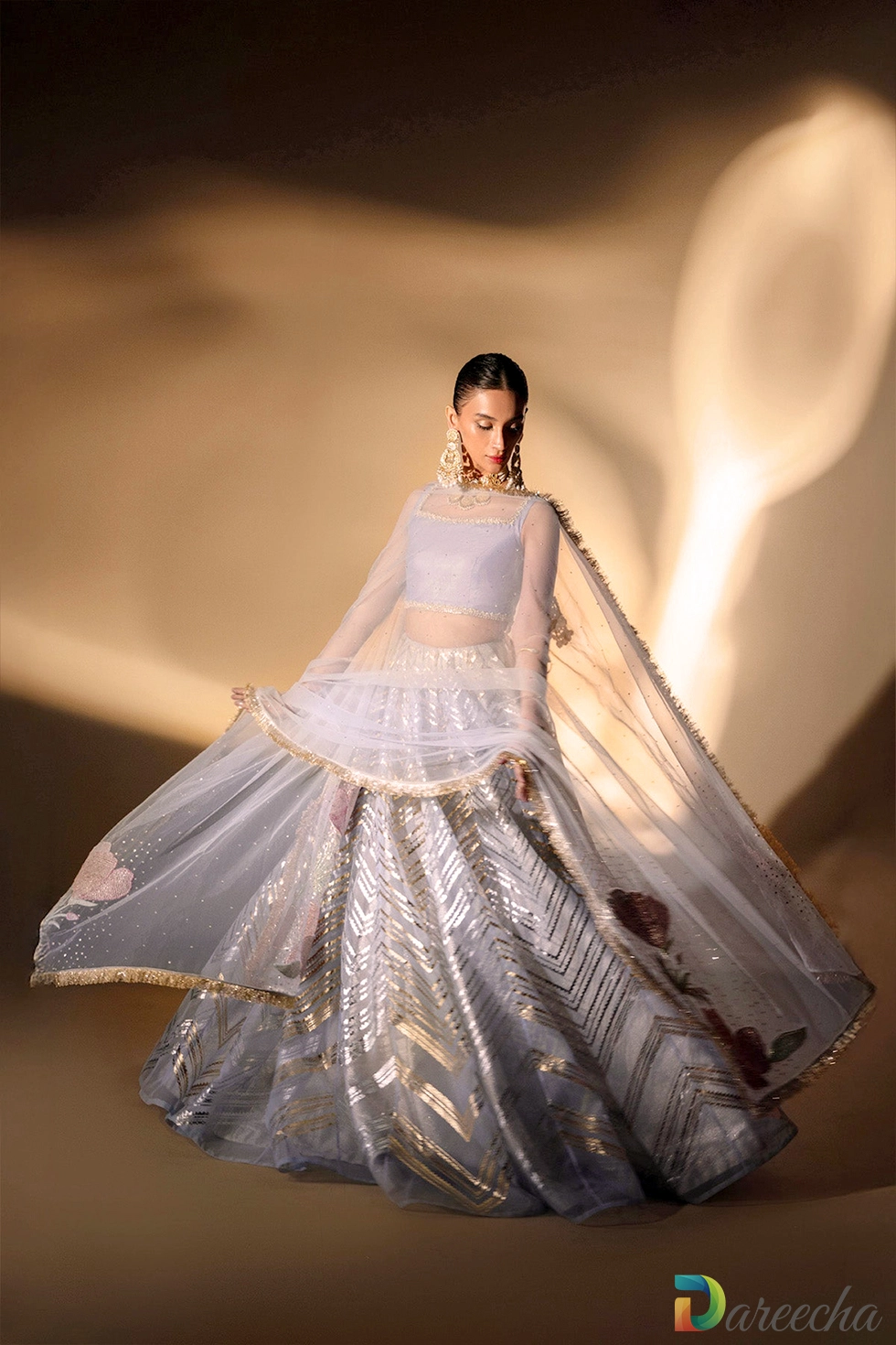 Dynamic twirling view displaying wide circular flare of periwinkle organza foil printed lehenga and floating net dupatta