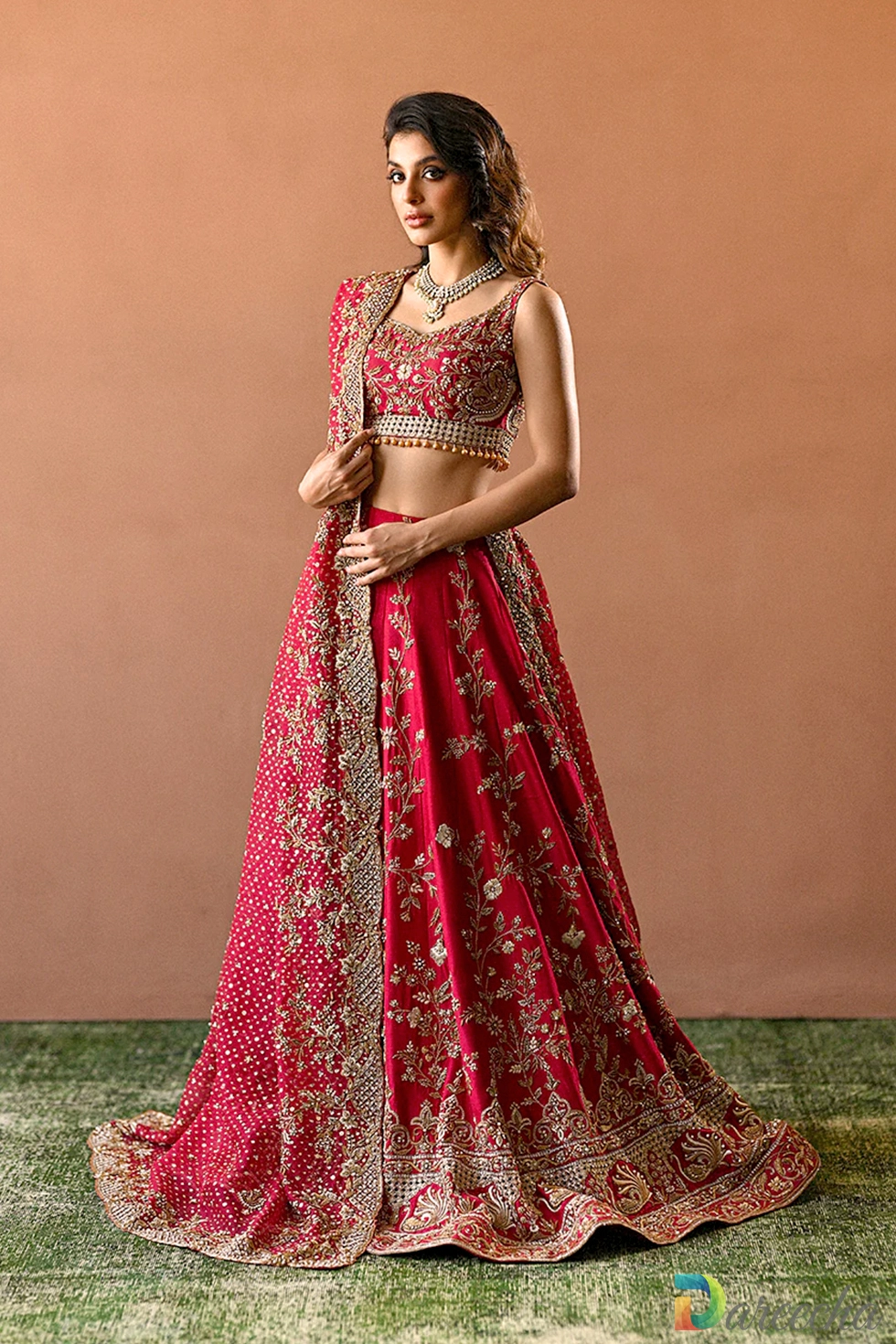 Full length standing pose of model in candy red raw silk bridal lehenga with draped organza dupatta