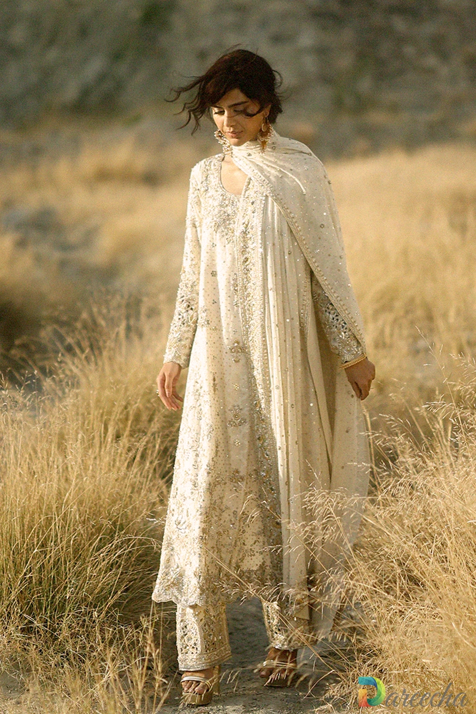 Full length outdoor view of model walking in the ivory hand embroidered long shirt showing the scalloped hem and embroidered izaar