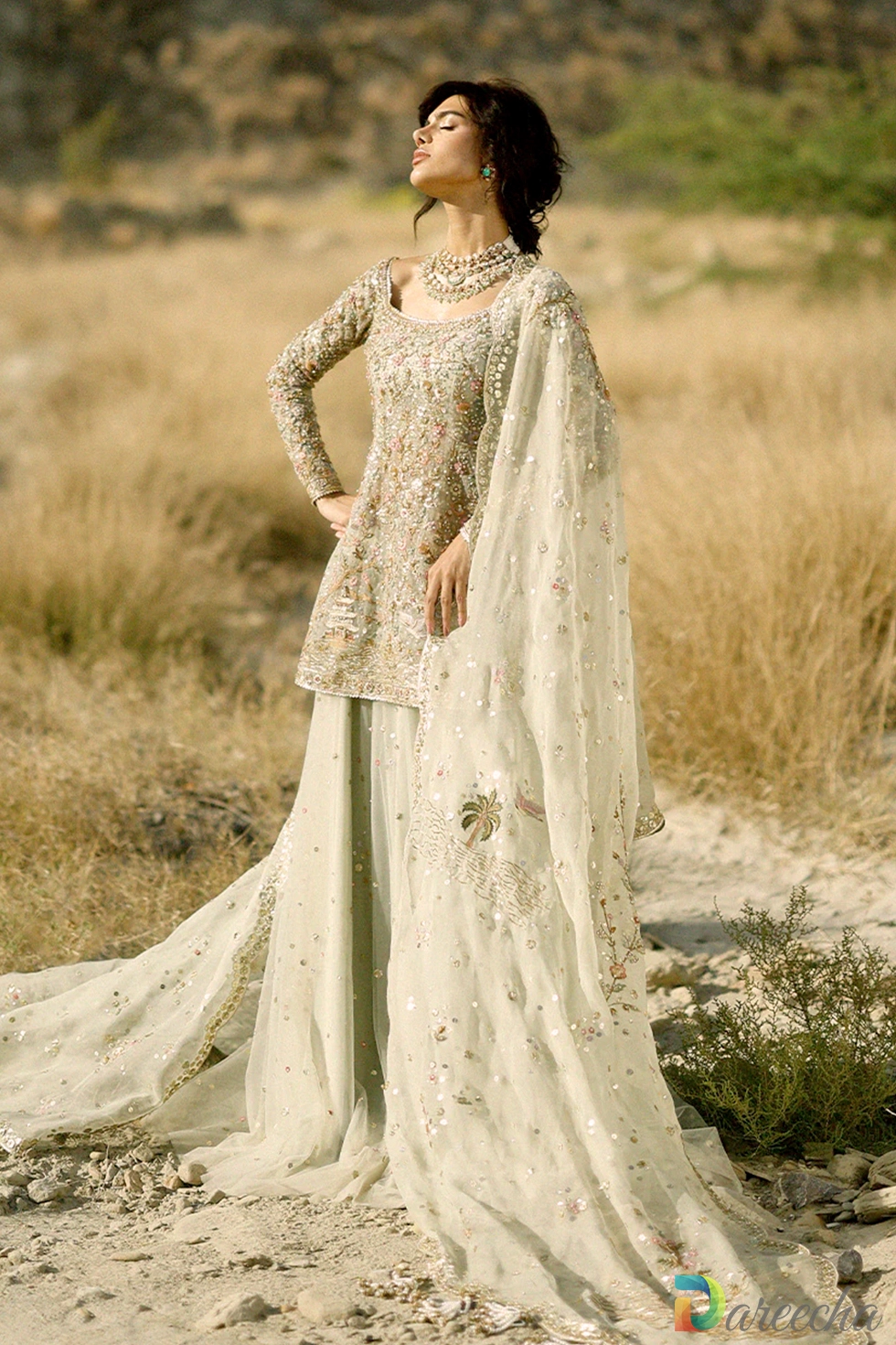 Full length standing portrait in desert setting of celadon tulle short shirt lehenga with draped veil
