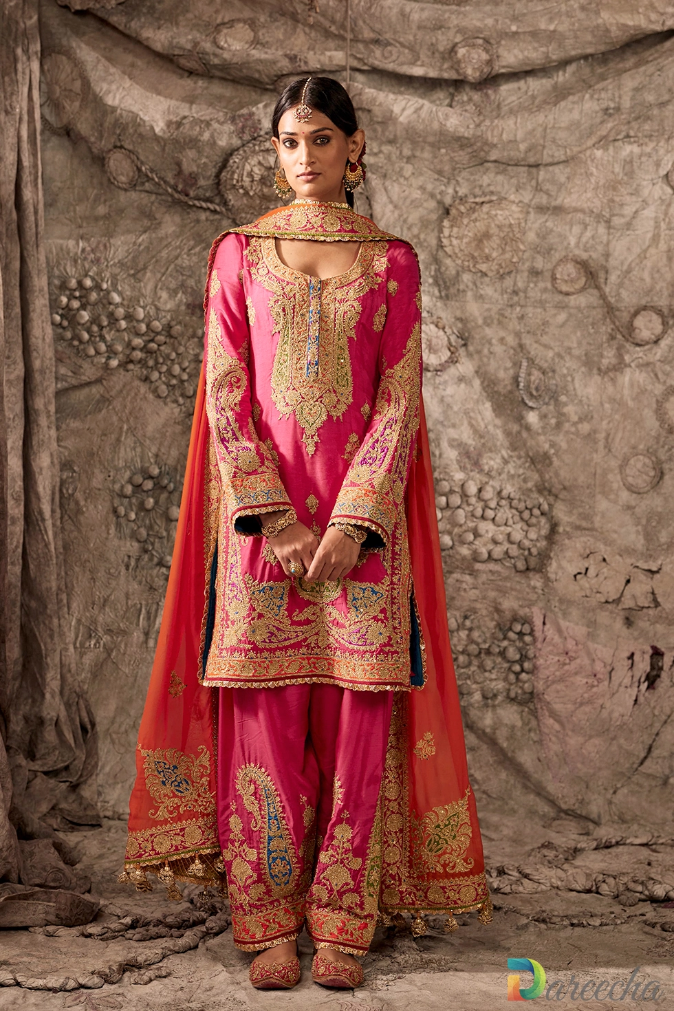Full length front view of model wearing fuchsia embroidered salwar kameez with flame orange organza dupatta and gold khussa shoes[cite: 18]