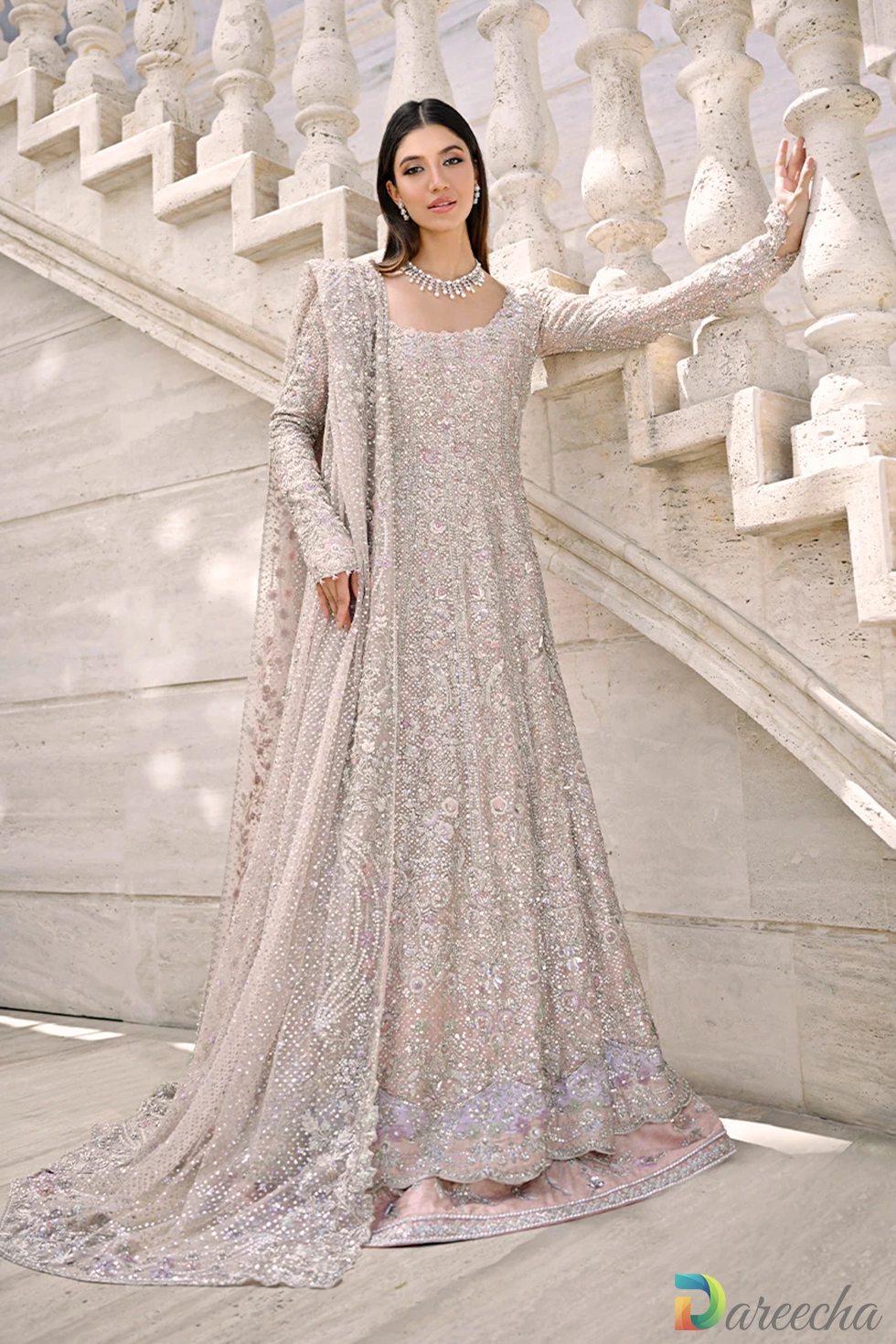 Full length front view of model on marble staircase wearing champagne pink peshwas lehenga with silver zardoze embroidery and draped tulle dupatta