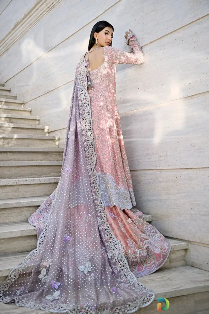 Back view on stairs highlighting long train and butterfly embroidery on rose quartz peshwas lehenga