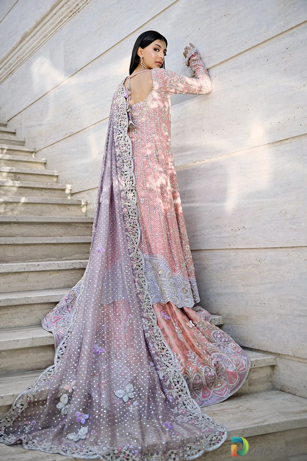 Back view on stairs highlighting long train and butterfly embroidery on rose quartz peshwas lehenga
