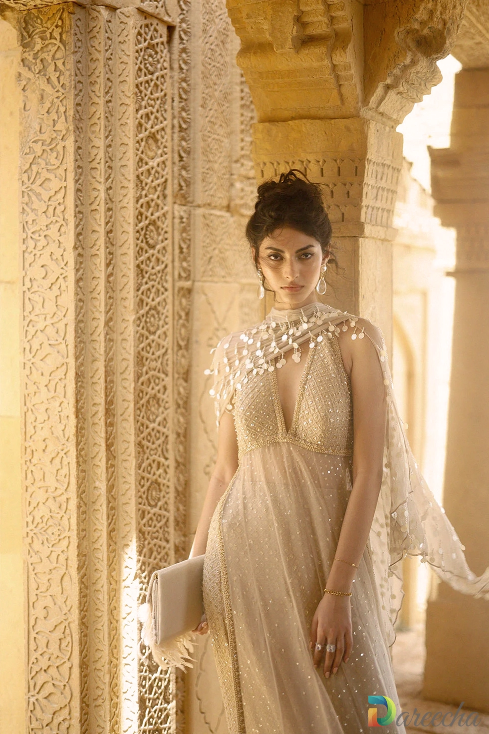 Close up portrait of model wearing halter neck top with metallic coin capelet on beige crinkle chiffon lehenga