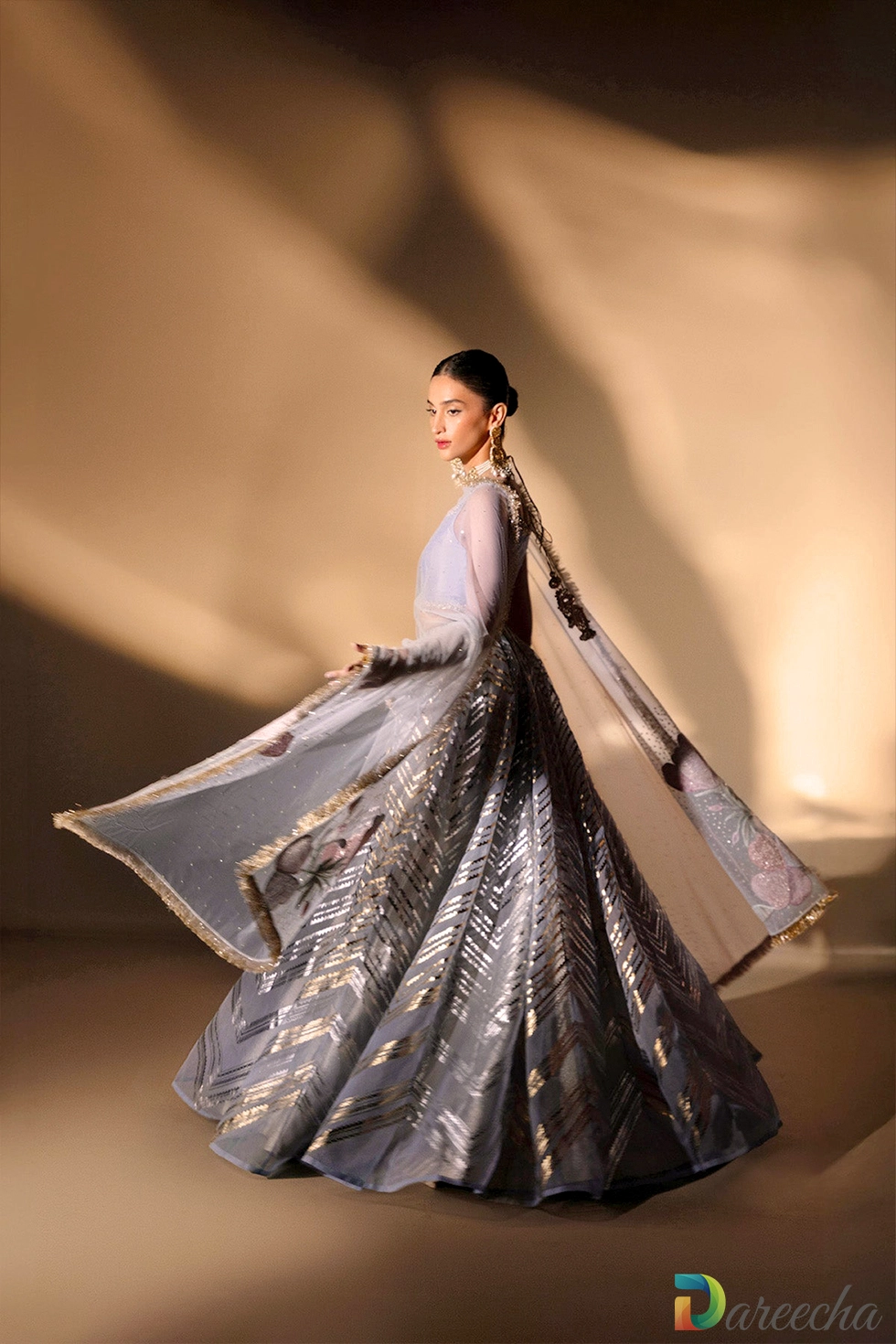 Model standing in periwinkle organza lehenga choli holding net dupatta featuring floral embroidered borders and kiran lace