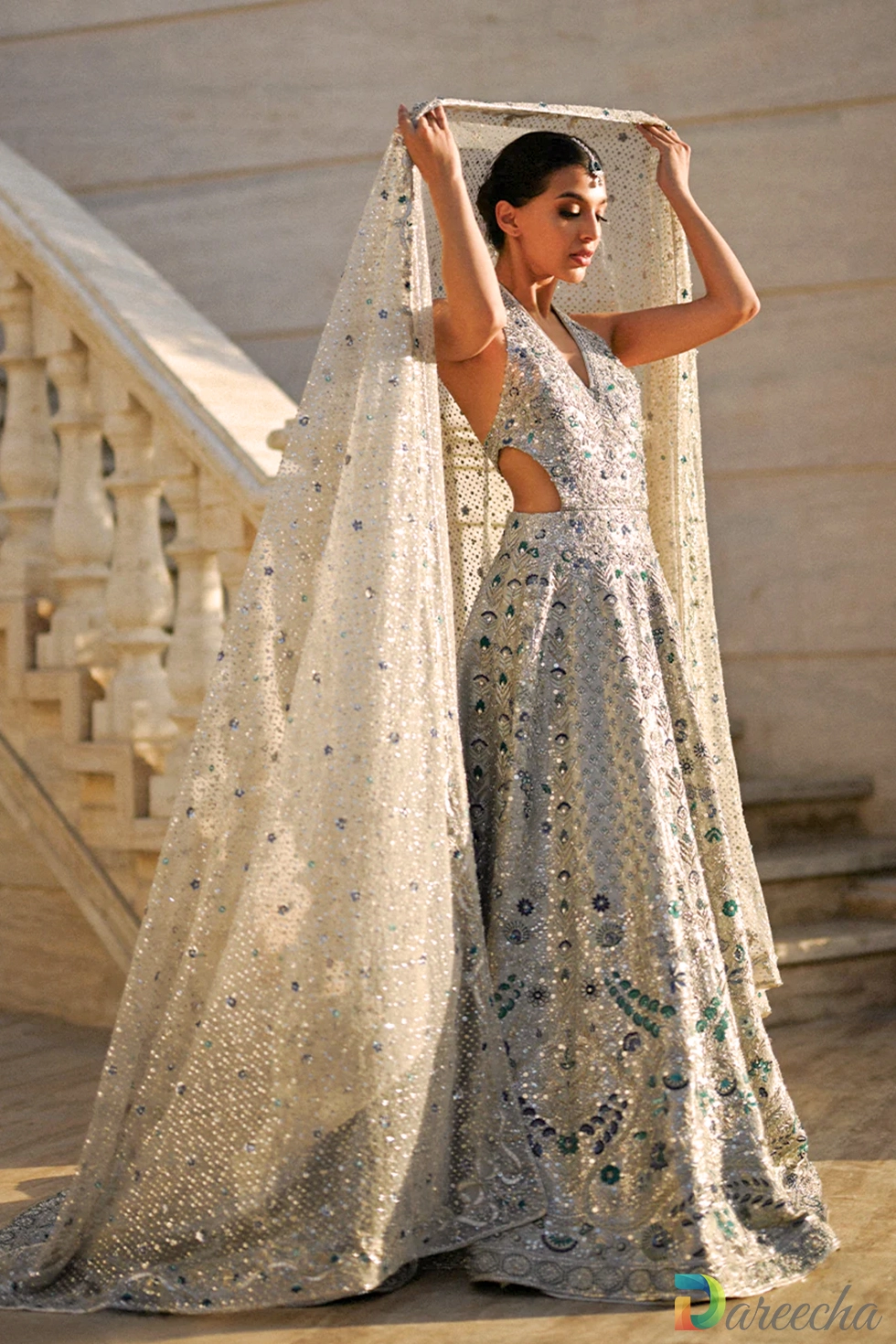 Model in an icy platinum backless bridal peshwas with geometric zardoze embroidery and halter back cutout.