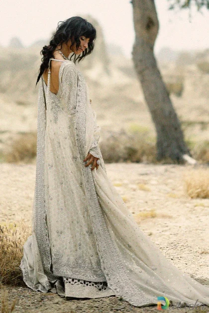 Model standing outdoors in ivory peshwas with dhaka pajama displaying draped tulle dupatta with scalloped zardoze border