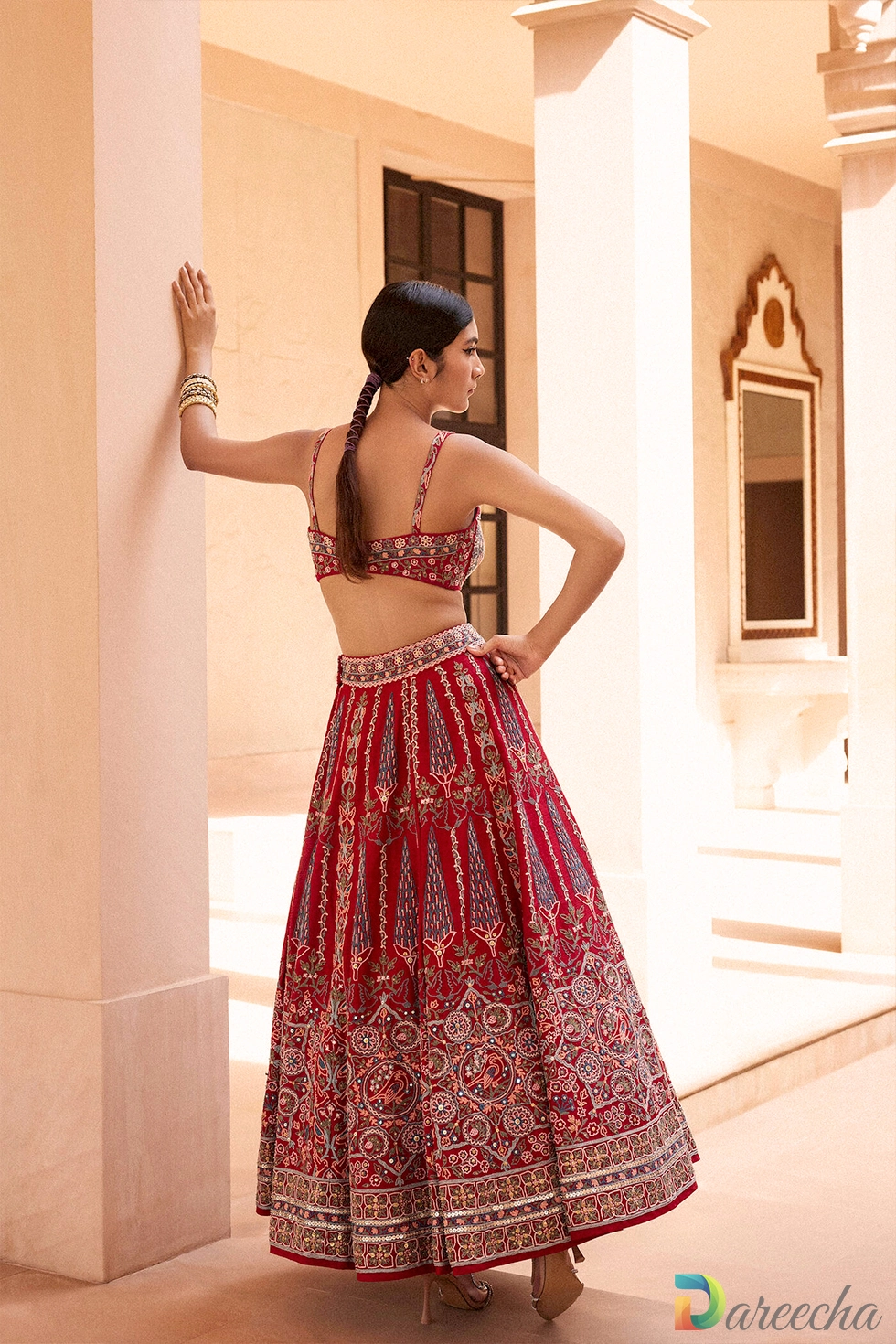 Back view of model wearing embroidered red matka silk bustier top showing strap detail and waistband embroidery