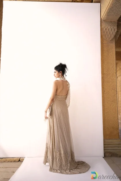 Full standing view displaying low open back and flowing layered skirt on beige crinkle chiffon lehenga