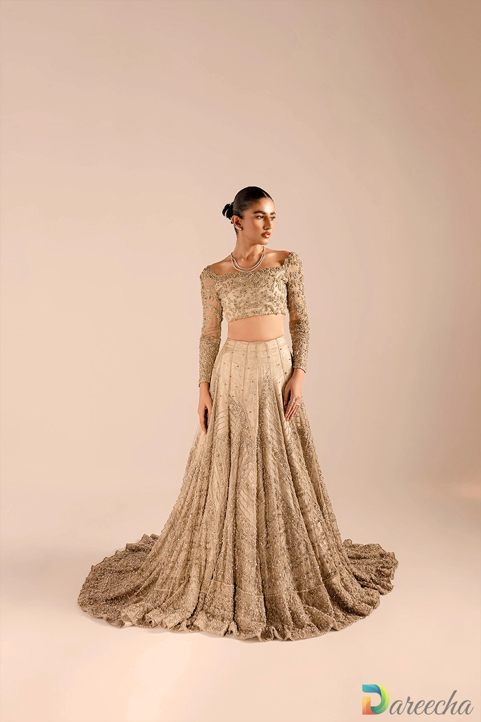 Front view of model in champagne kundan net lehenga choli displaying scalloped neckline and full embellished sleeves