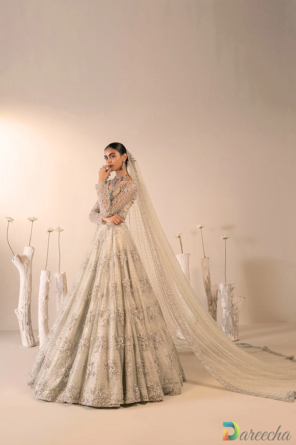 Profile view of model standing in mint green embellished net lehenga with long sheer embroidered veil cascading behind