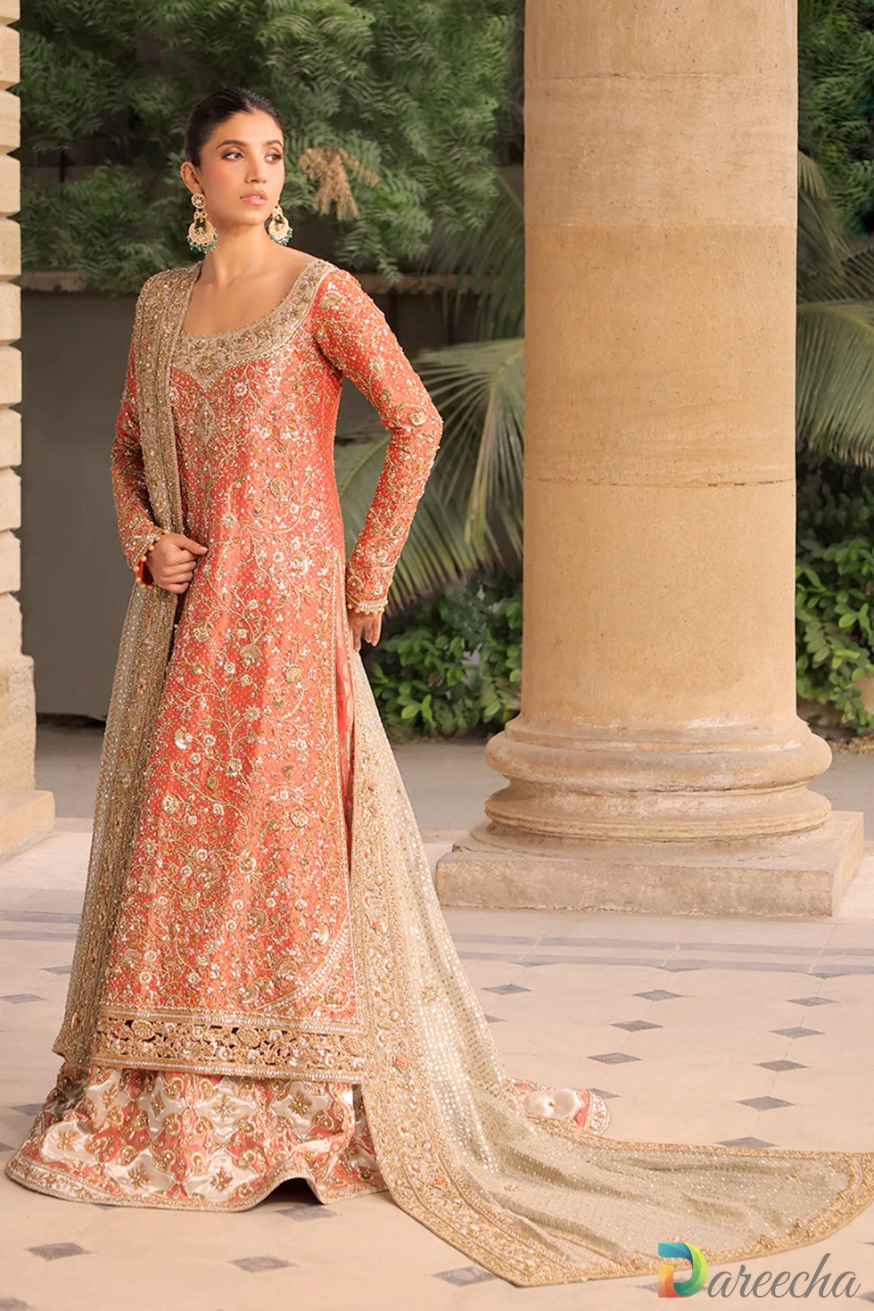 Model wearing coral tissue A line long shirt lehenga set standing between sandstone pillars in full view