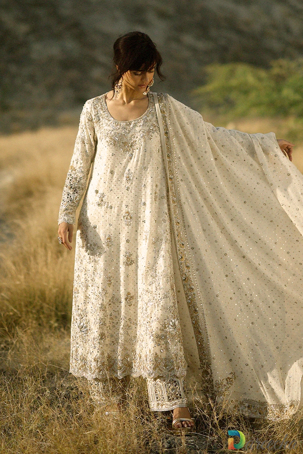 Full length front view of model wearing the ivory hand embroidered long shirt with raw silk izaar trousers and flared net dupatta
