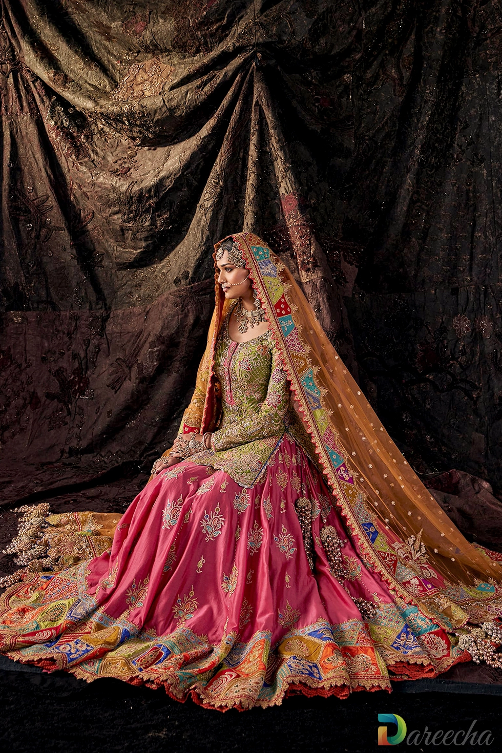 Seated view showing wide sweeping fuschia lehenga skirt with multi colored geometric chatta patti hemline border[cite: 11]