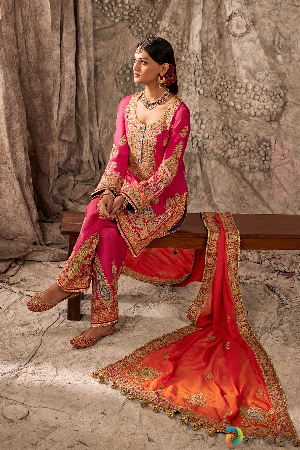 Side profile view of seated model displaying long sleeves with intricate gold tilla embroidery and heavily embroidered fuchsia salwar cuffs