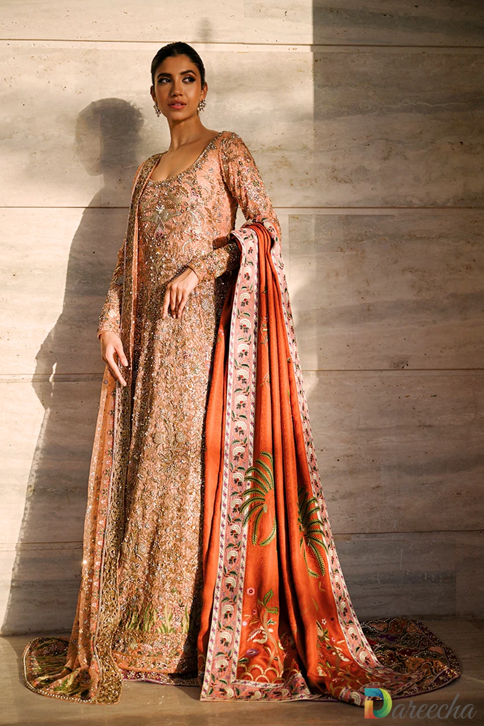 Full length standing view against stone wall showing coral peshwas with hand embroidered tangerine shawl displaying palm and peacock borders[cite: 22]
