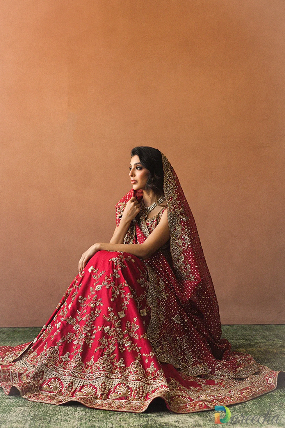 Seated full length shot of model in candy red raw silk bridal lehenga showing peacock figurines and cutwork arches[cite: 33]