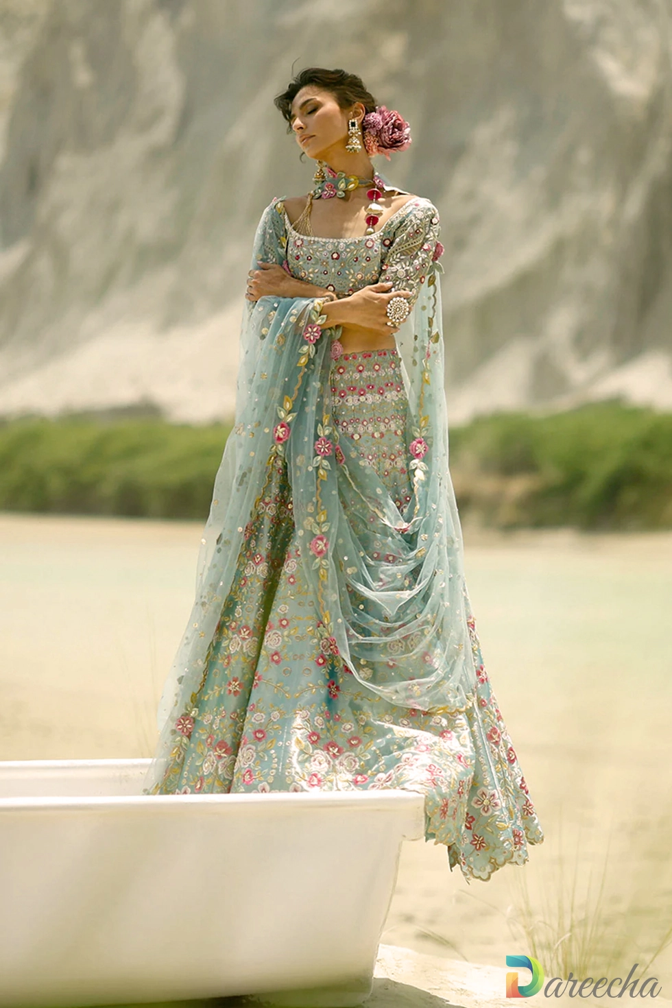 Model wearing ice blue tissue lehenga with blush pink and magenta floral embroidery in outdoor boat setting