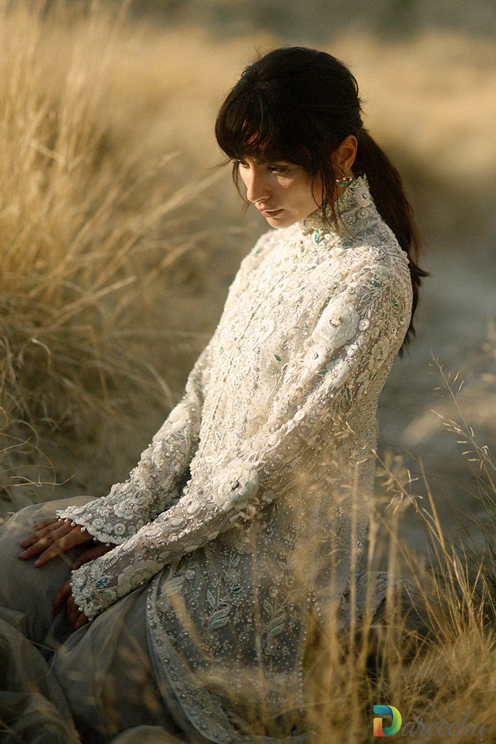 Seated pose highlighting intricate zardoze embroidery on sleeves of champagne tulle peshwas