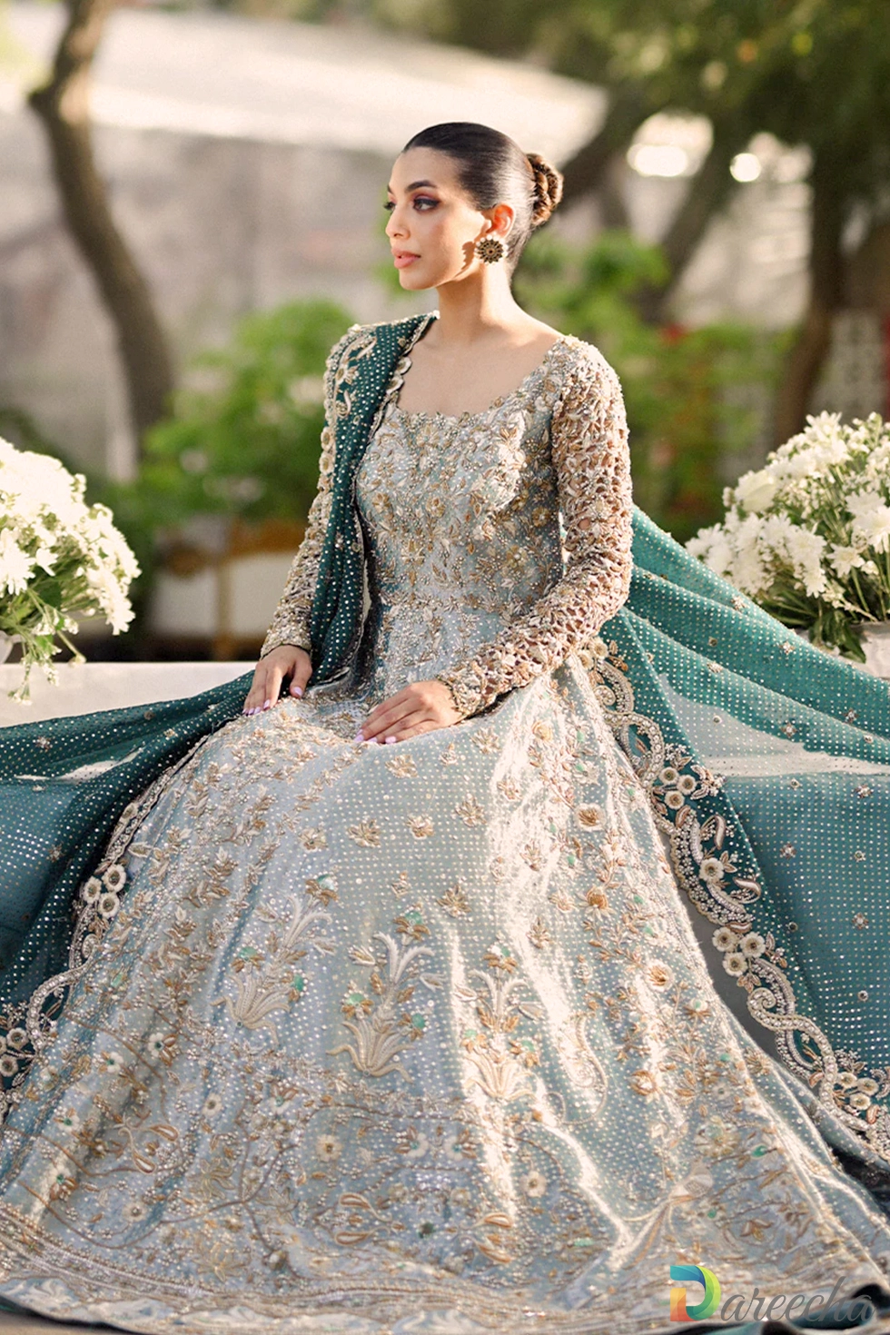 Seated angle of mint green tissue peshwas showing intricate resham floral jaal and spread out tissue skirt