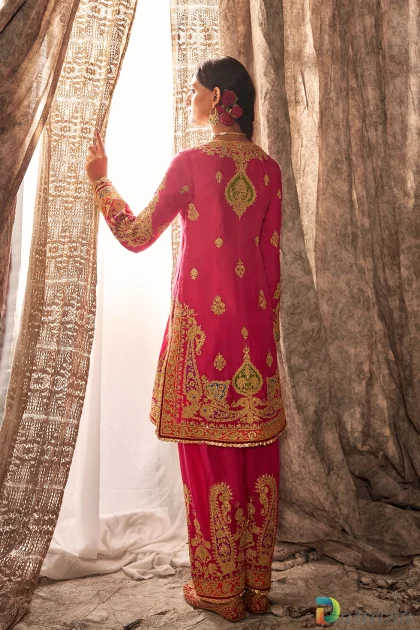 Full length back view of model standing by lace curtain showcasing gold embroidered paisley medallion on fuchsia pink kurta and embroidered salwar pants[cite:
