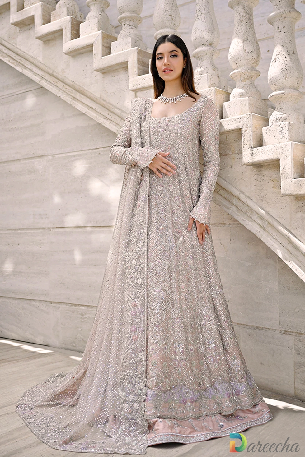 Medium front portrait of model standing on marble stairs displaying detailed zardoze and resham embroidery on bodice and full sleeves