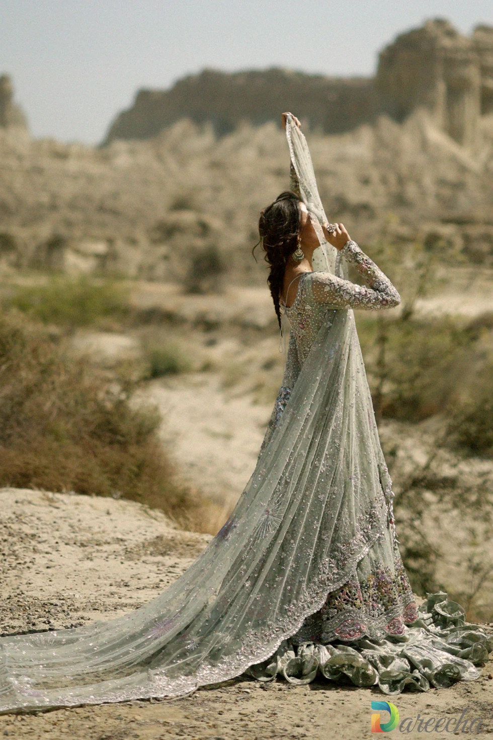 Full length profile view of model holding up long sheer dupatta of frosted mint peshwas lehenga in desert setting[cite: 26]