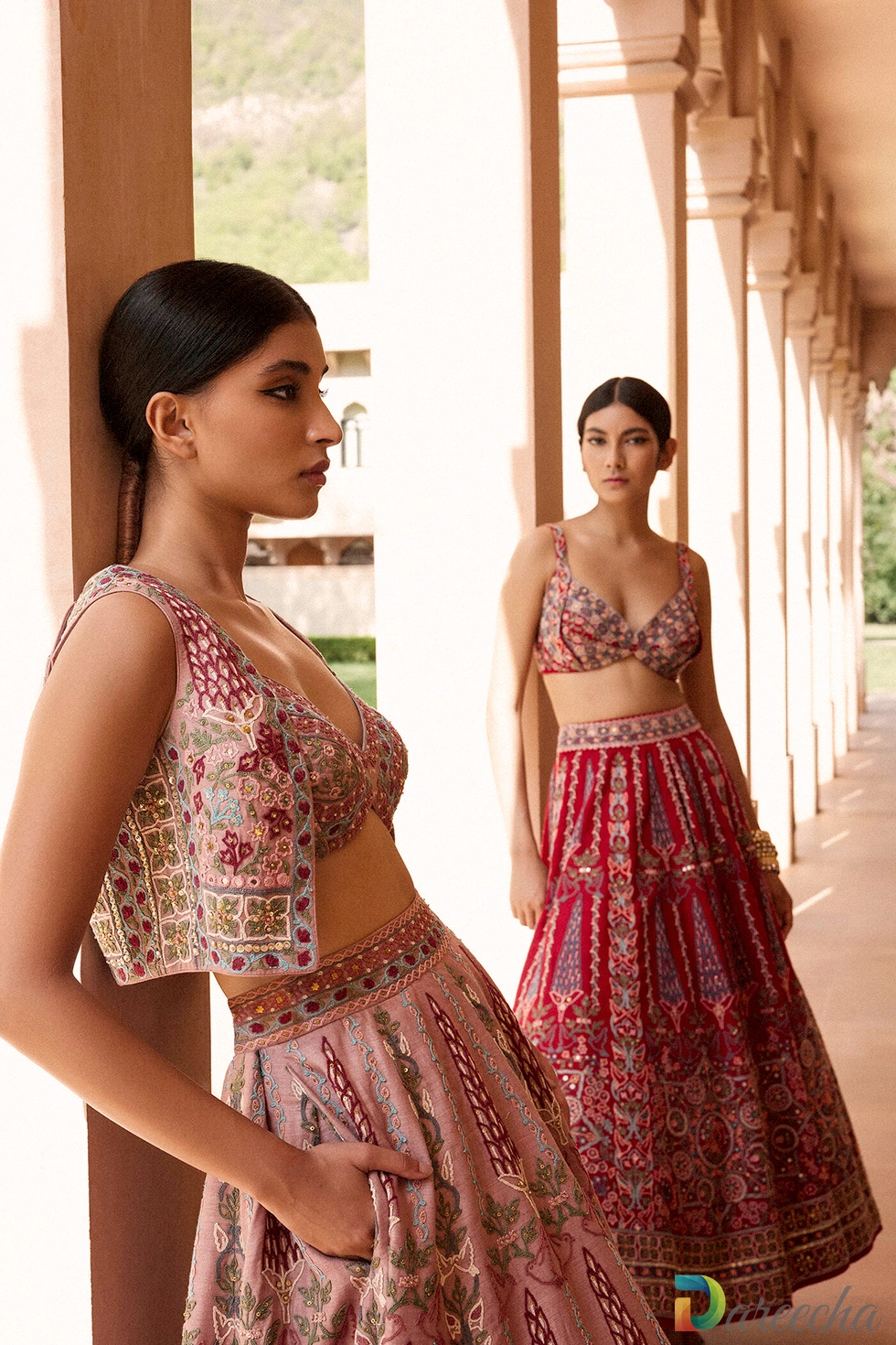 Side profile portrait of model leaning against sandstone pillar wearing dusty rose matka silk crop jacket and lehenga