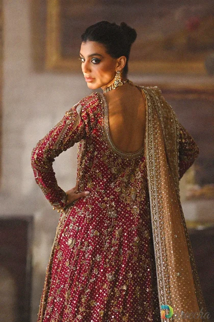 Dramatic standing pose of model in crimson bridal peshwas lehenga looking back with draped copper dupatta