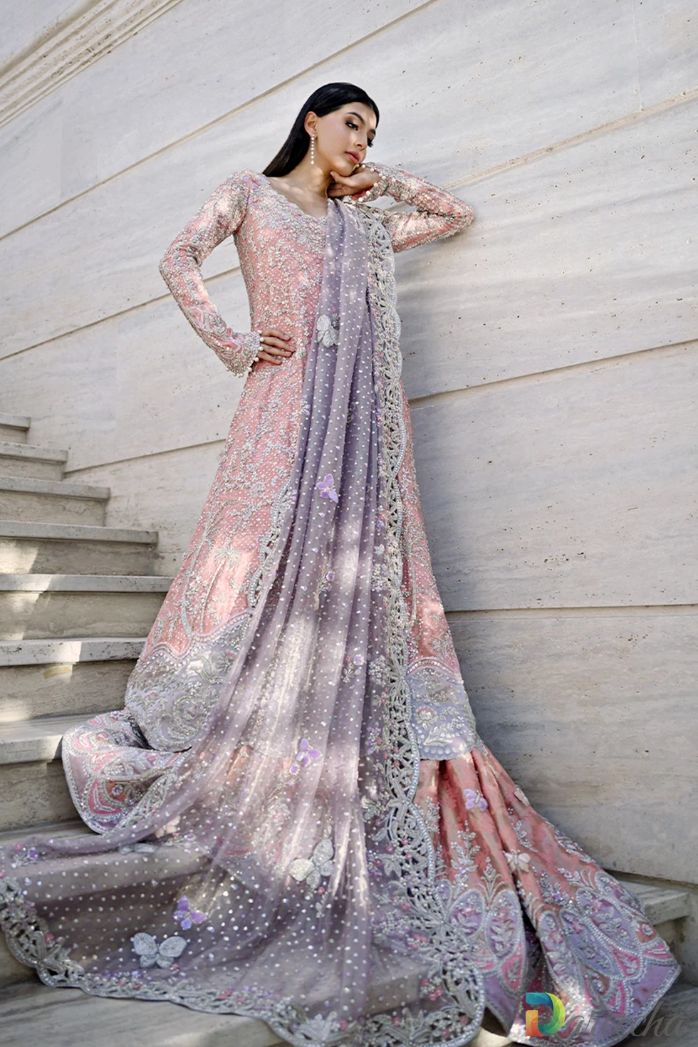 Leaning pose against stone wall showing intricate zardoze detailing on rose quartz peshwas lehenga