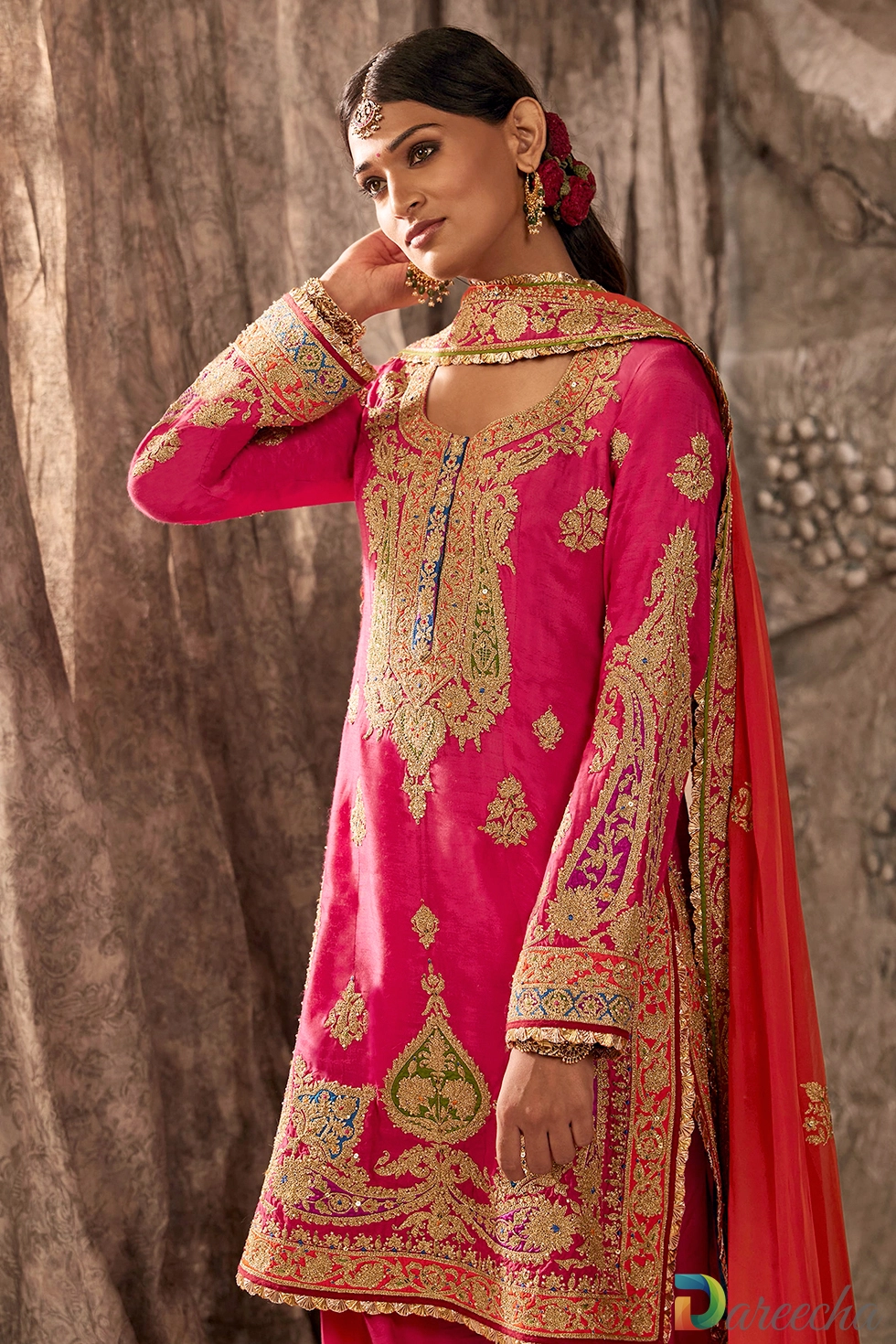 Side profile view of seated model displaying long sleeves with intricate gold tilla embroidery and heavily embroidered fuchsia salwar cuffs