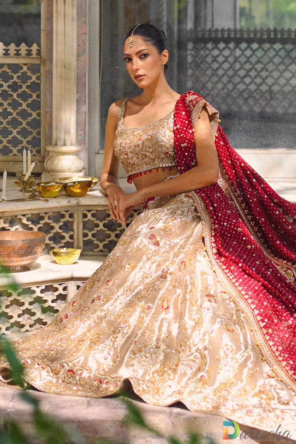 Seated portrait of model wearing gold tissue lehenga choli on marble steps in ornate courtyard[cite: 20, 24]