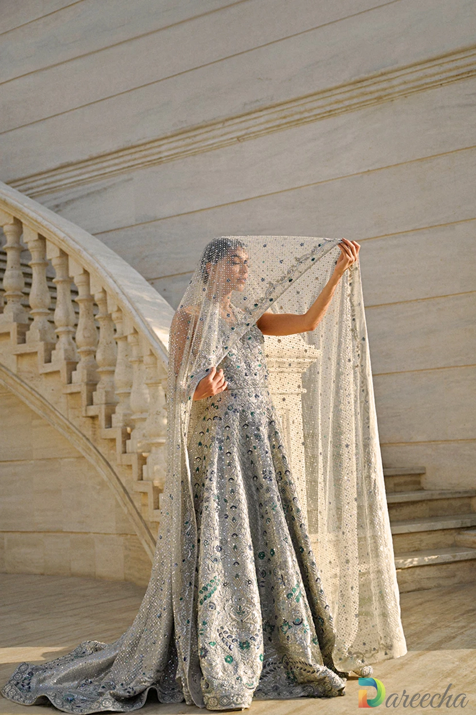 Front view of slim fit silver bridal peshwas showing halter neckline and emerald resham floral details with tulle dupatta veiled over head.