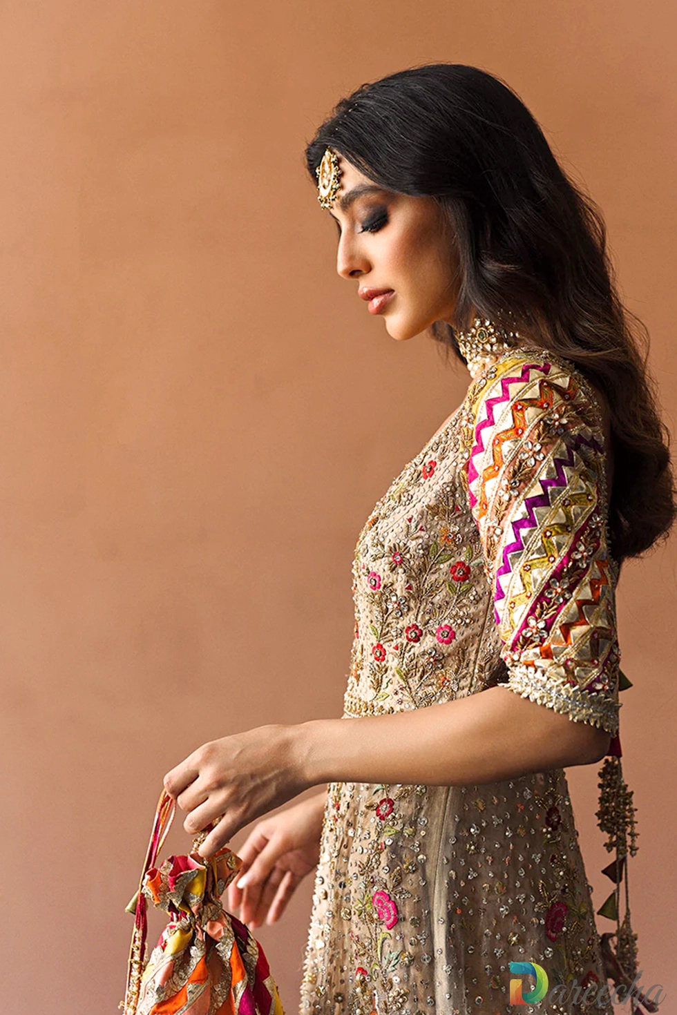 Side profile view of copper tissue bridal peshwas showing intricate multi-hued sleeve embroidery and potli pouch