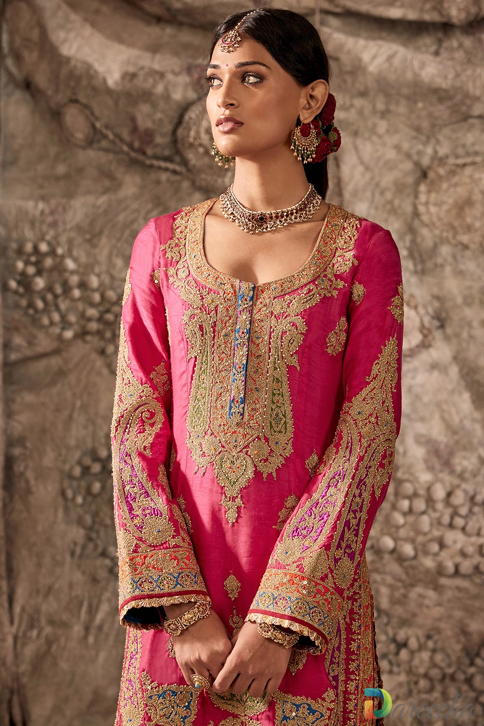 Close up portrait of model wearing fuchsia pink silk kurta with gold tilla embroidery, blue neckline placket accent, and statement bridal jewelry