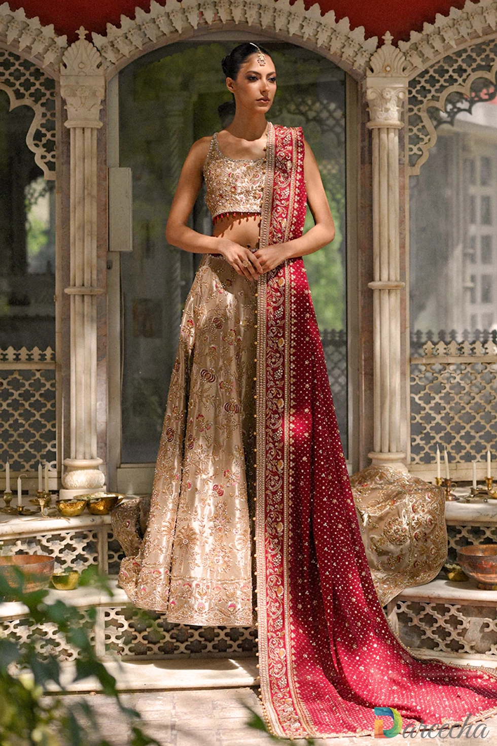 Full length portrait of model wearing gold tissue lehenga choli set framed by traditional sandstone pillars[cite: 20, 25]