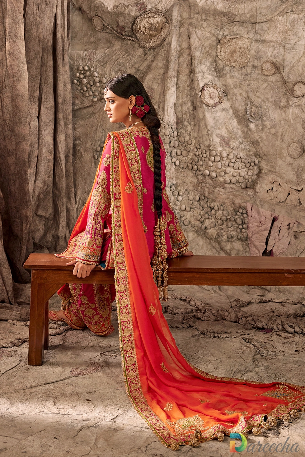 Three quarter standing view of model in fuchsia pink embroidered kurta and salwar set with flame orange organza dupatta draped over shoulders[cite: 15]