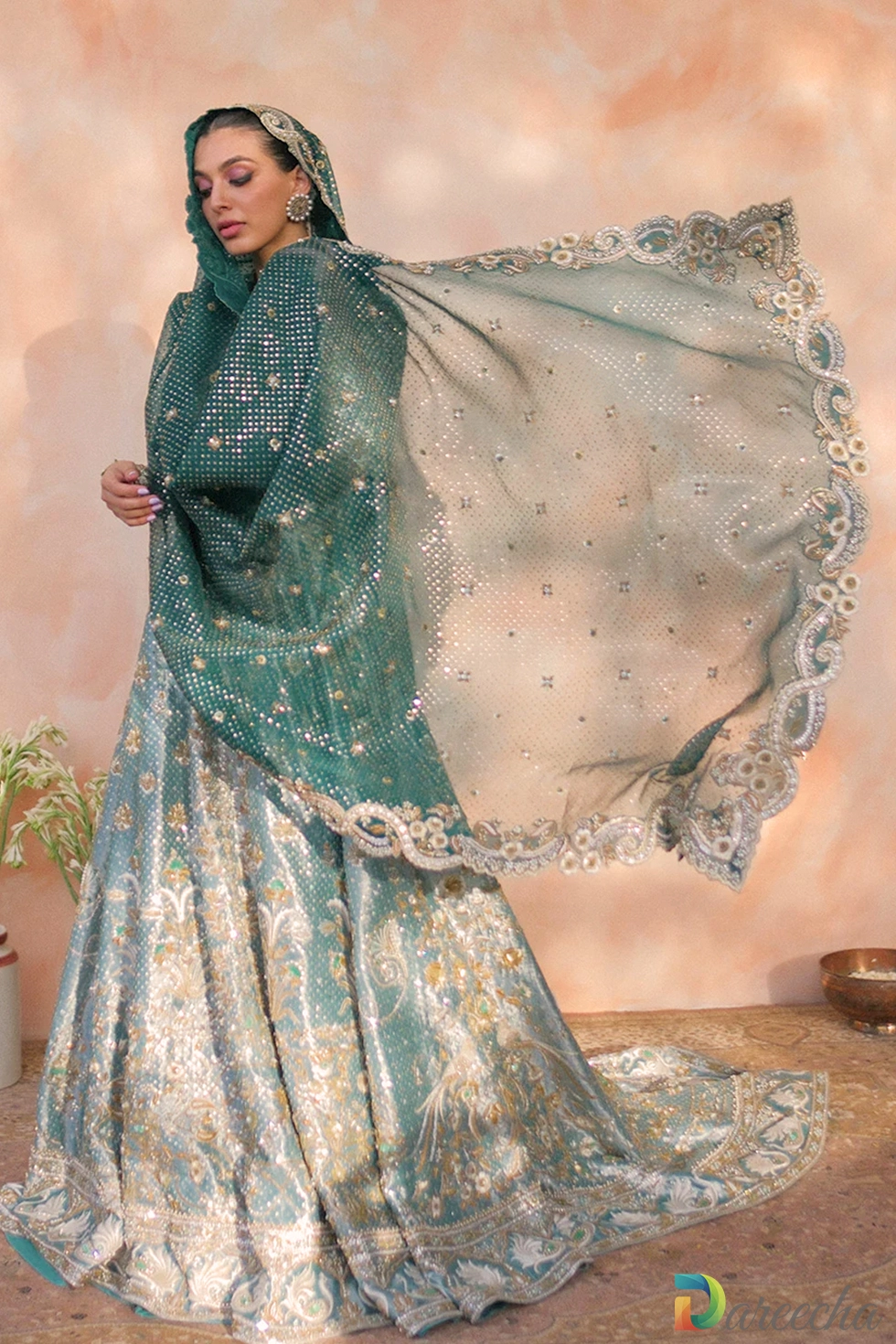 Three quarter angle view of mint green tissue peshwas leaning on stone pillar with draped emerald dupatta