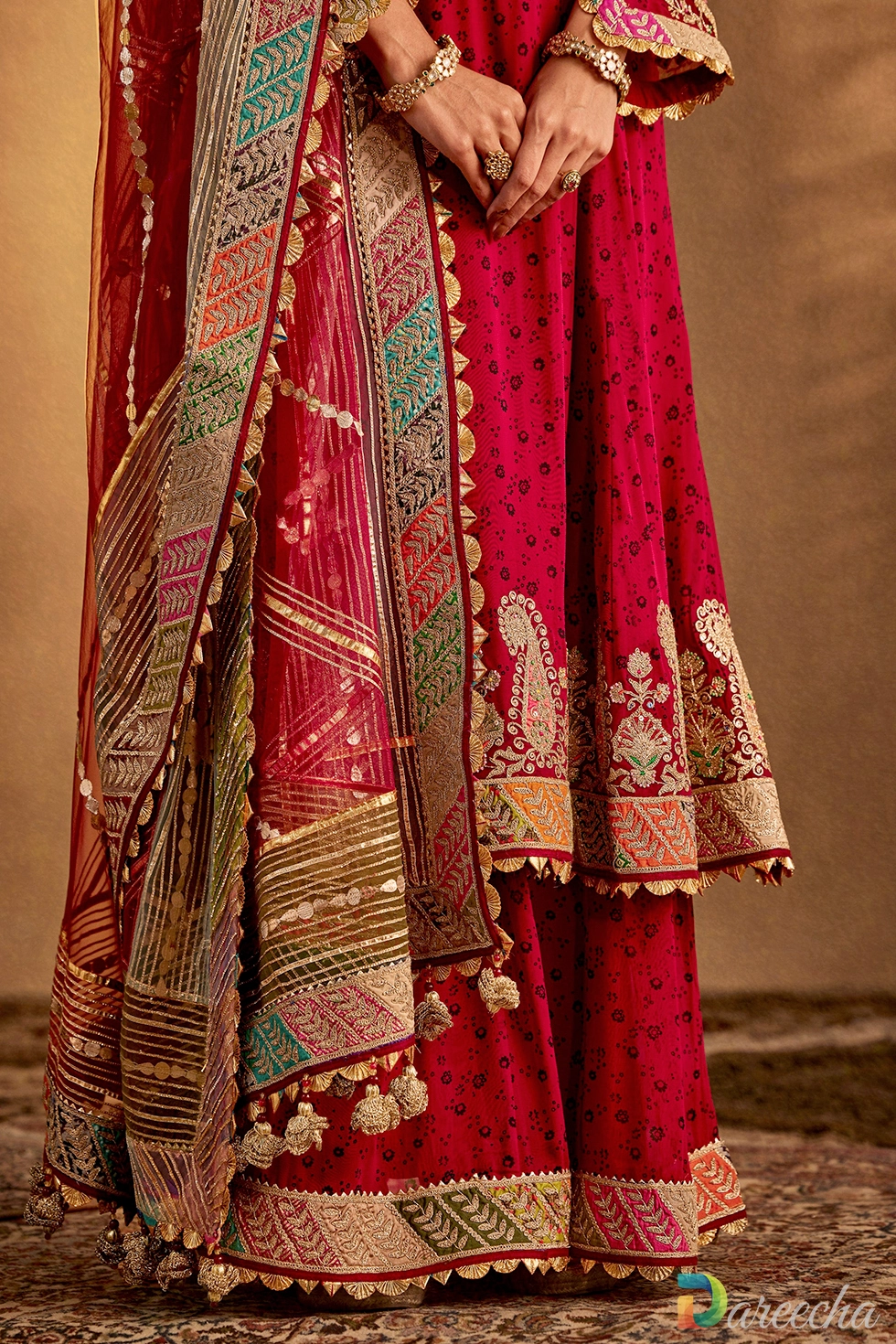 Close-up of rich marodi embroidery, pearls, zardozi work, and chevron borders on a maroon silk kurta hem.